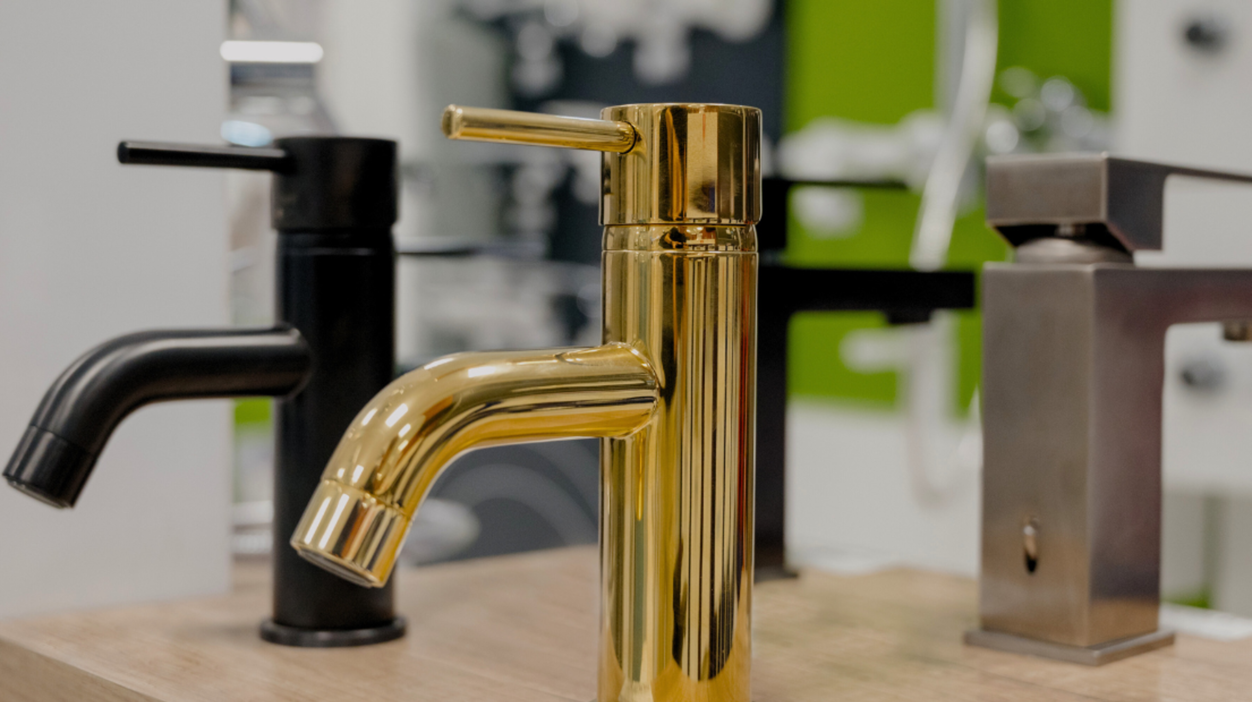 A display of modern water faucets in black, gold, and metallic finishes on a showroom counter. 