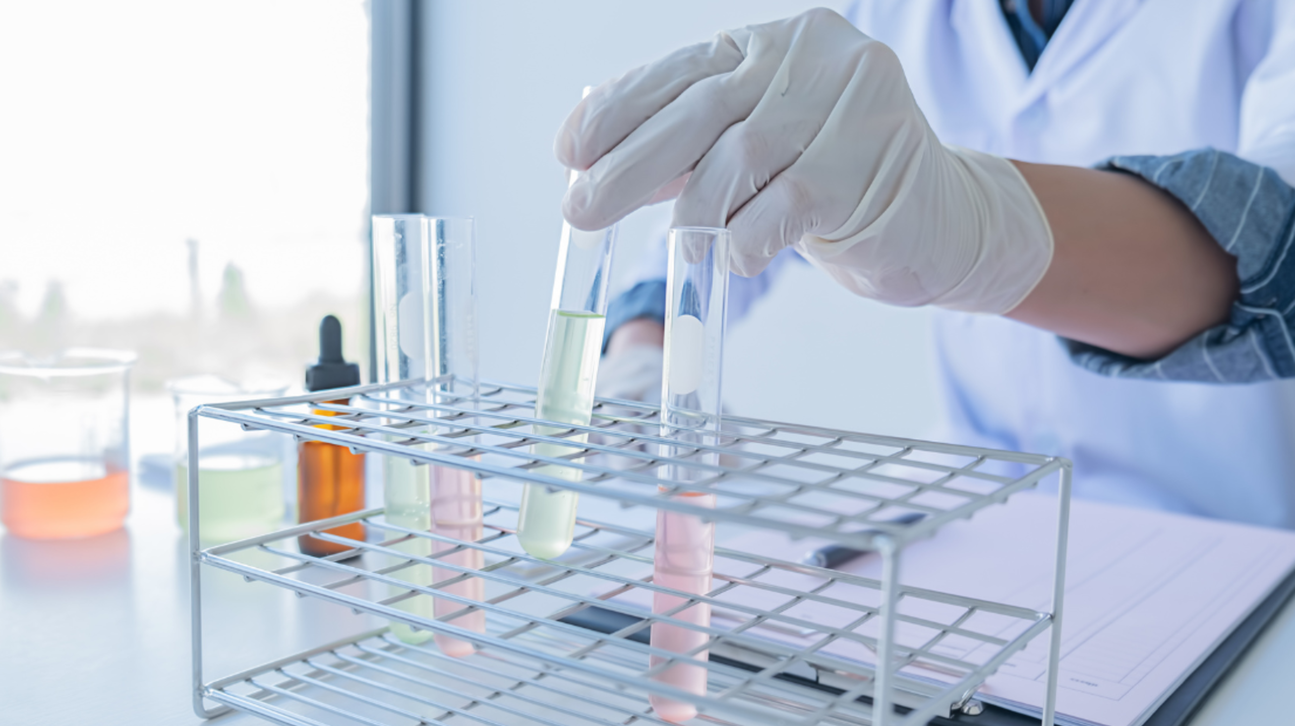 Eine Wissenschaftlerin oder ein Wissenschaftler mit Handschuhen hantiert mit Reagenzgläsern mit farbigen Flüssigkeiten in einem 