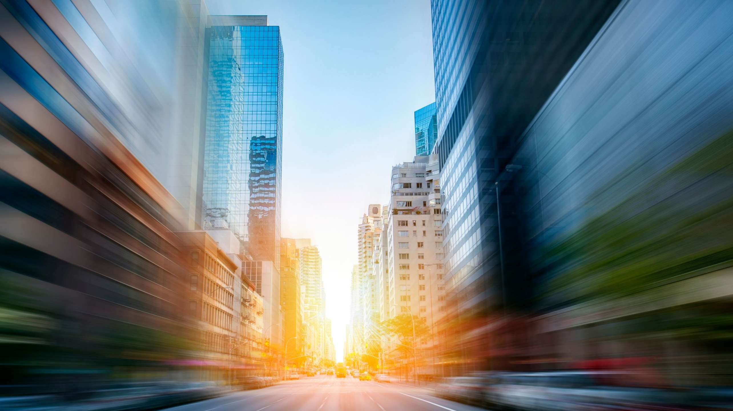 City street with tall buildings, motion blur, and bright sunlight ahead.